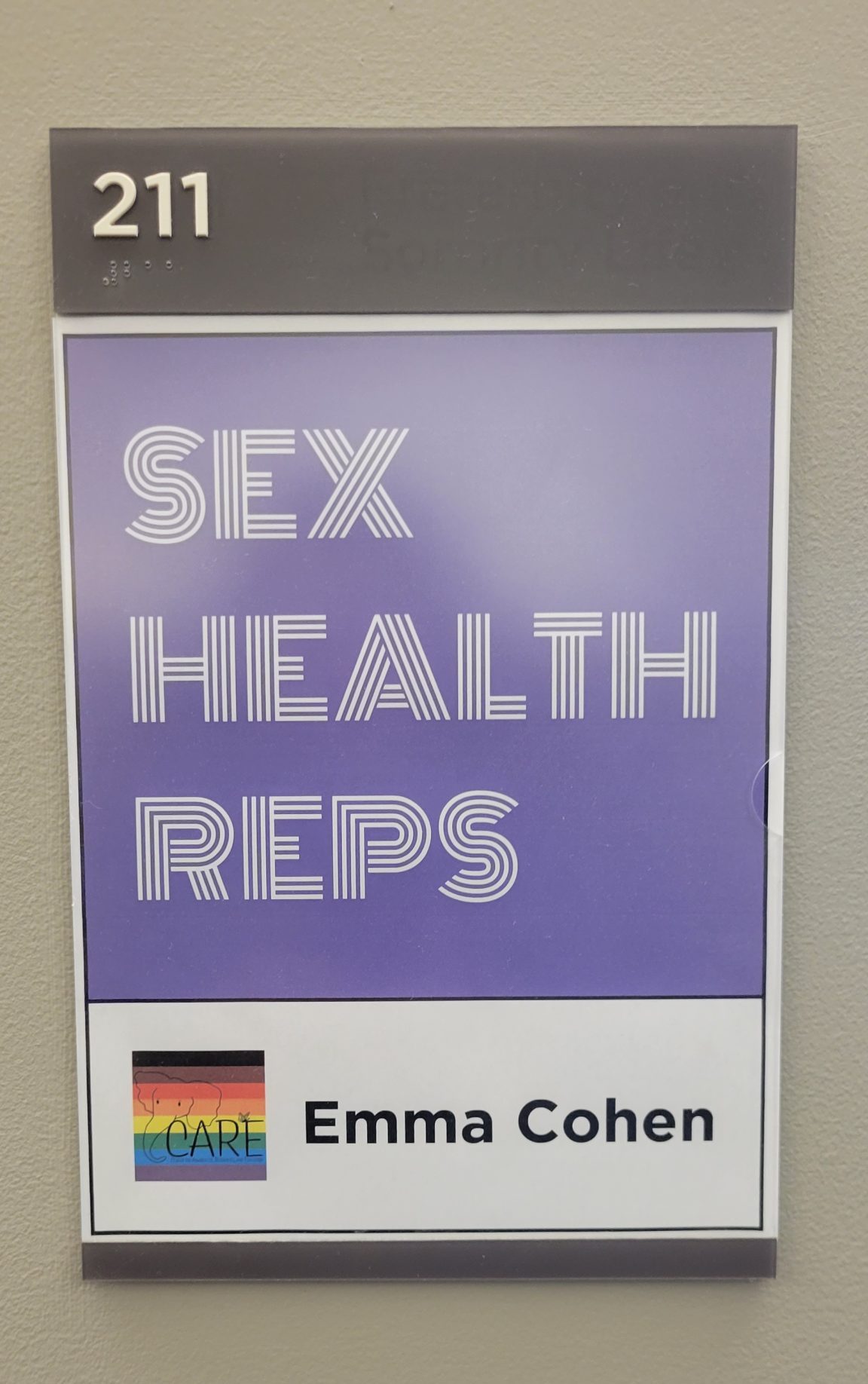 Purple sign that says Sex Health Reps. Underneath on a white background it says Emma Cohen.