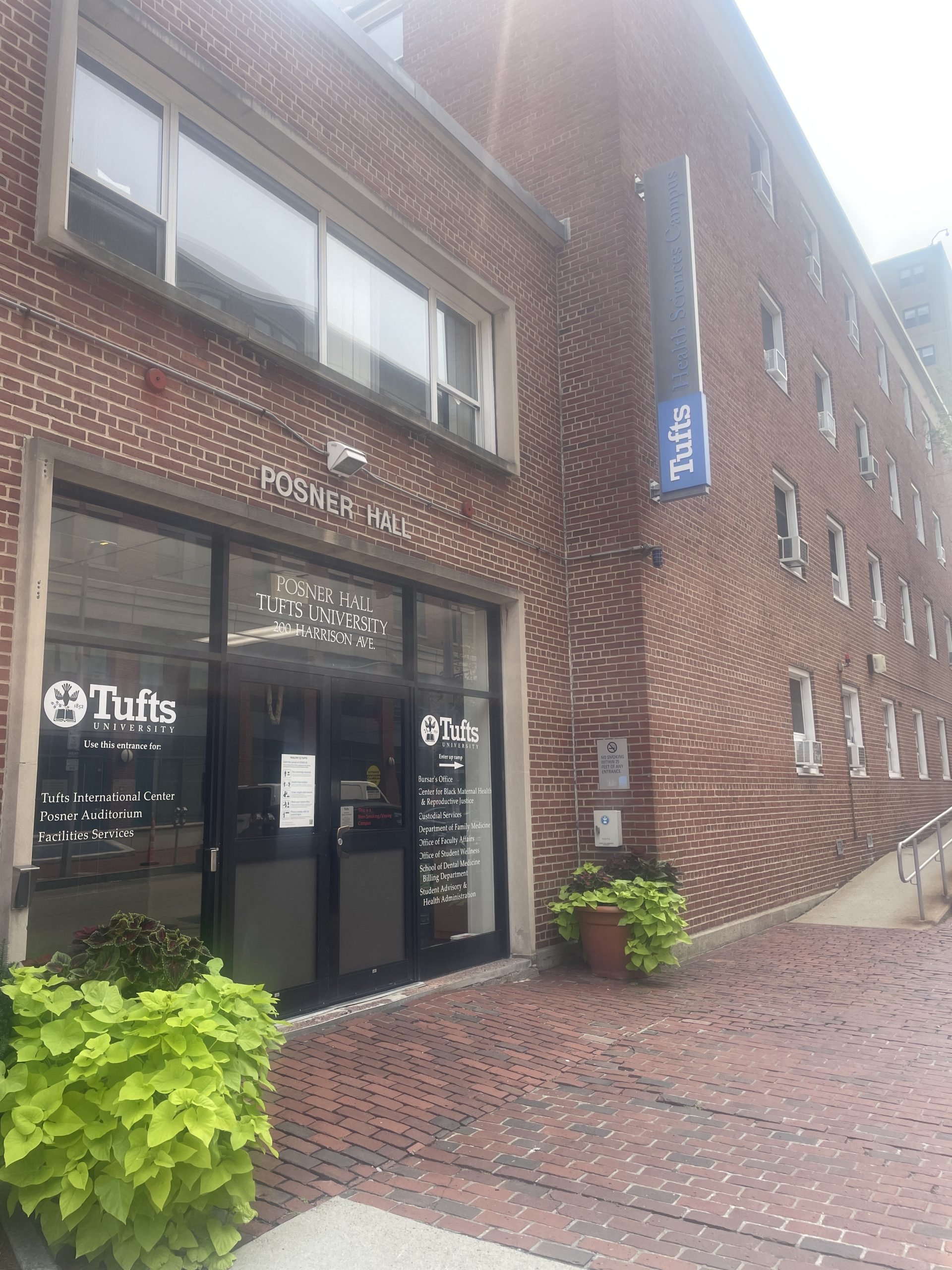 Brick building on a city block with a black door on the right of the image and a ramp leading to another door on the left of the image